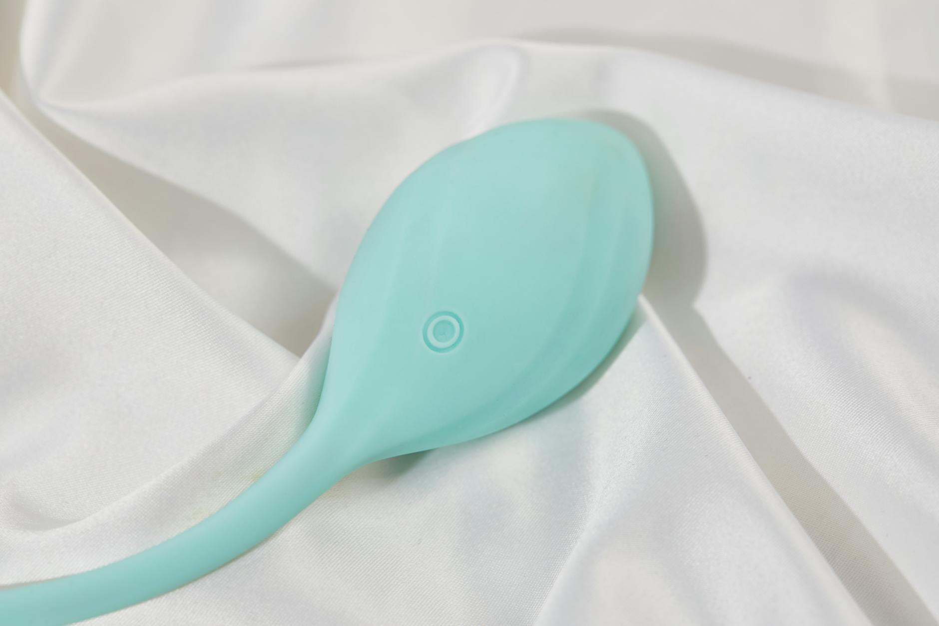 A hand holding a silicone clitoral vibrator against a purple background