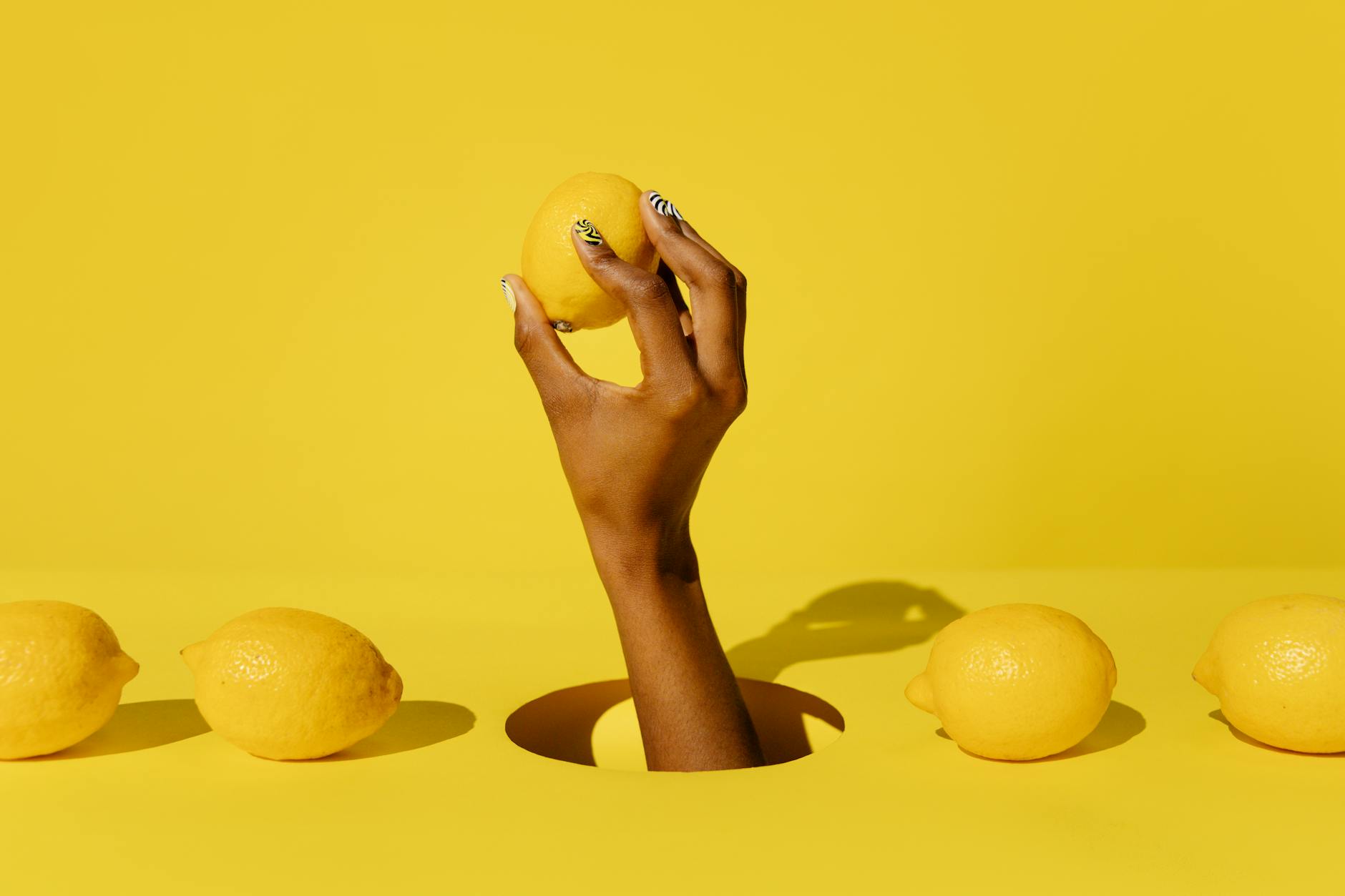 A hand holding a fresh lemon against a bright yellow background, symbolizing renewed energy and freshness