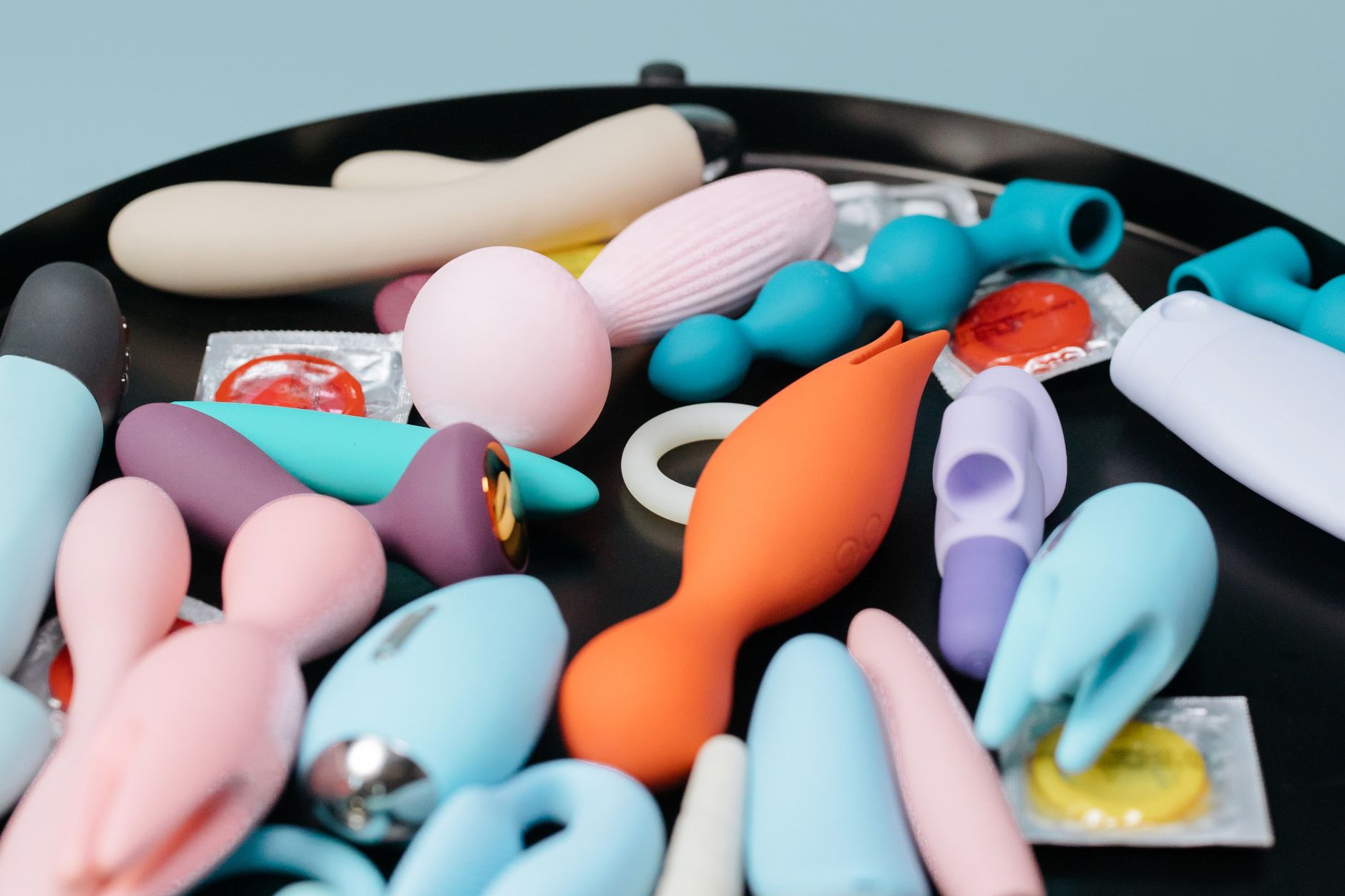 Two hands holding pink and blue silicone vibrators against a pastel background