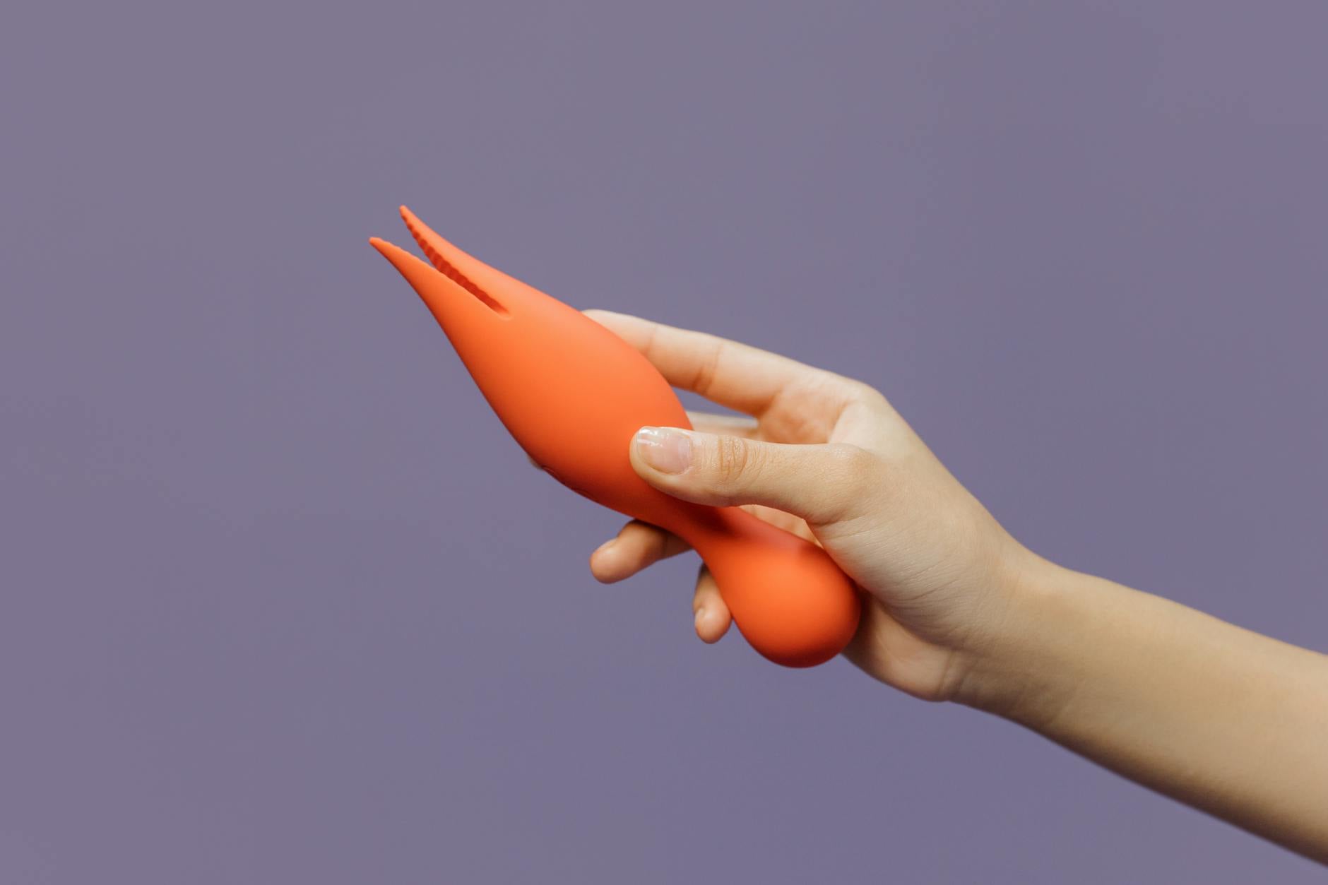 A hand holding an orange vibrator against a minimalistic purple backdrop, showcasing modern sensuality.