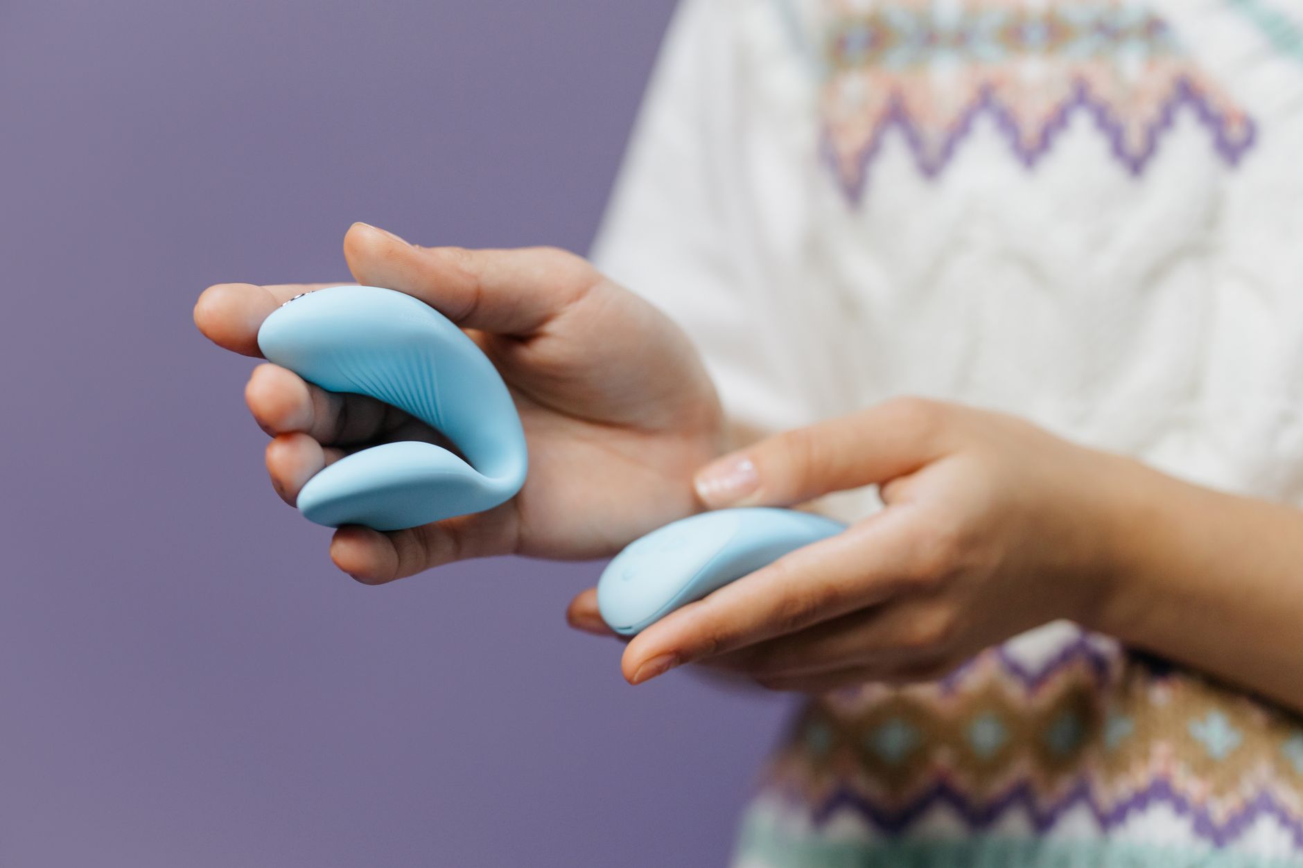 Close-up of hands holding a sleek blue lemon vibrator against a purple background