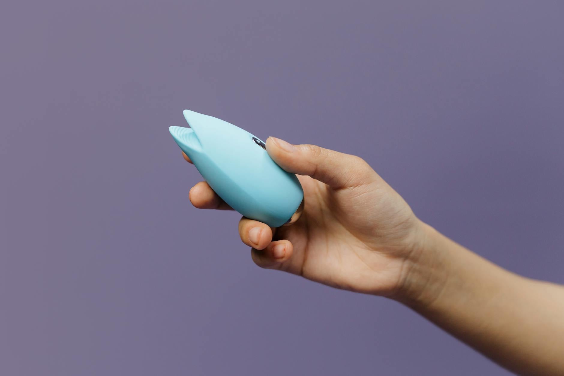 A blue silicone sex toy held in hand against a solid purple background
