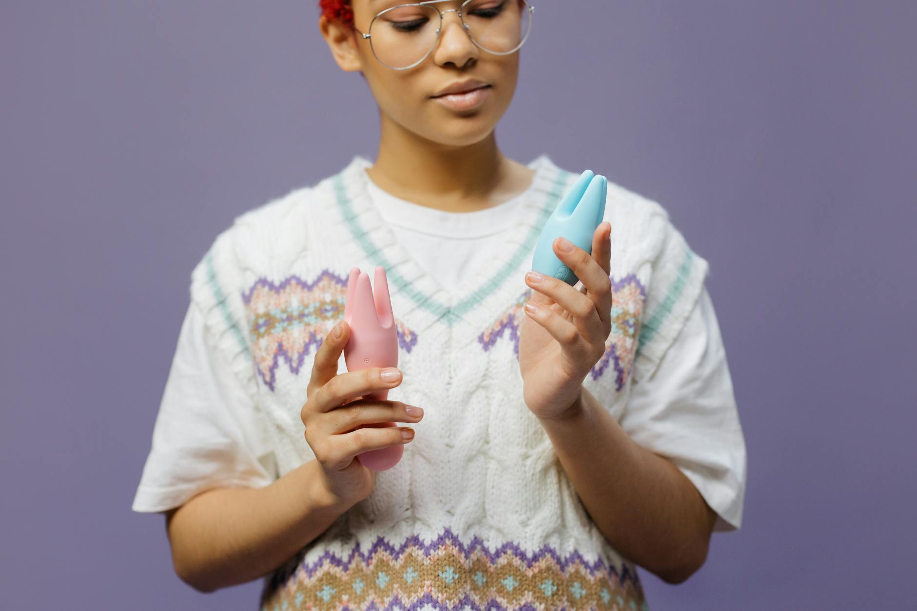 Woman holding blue and pink silicone vibrators in a contemplative manner