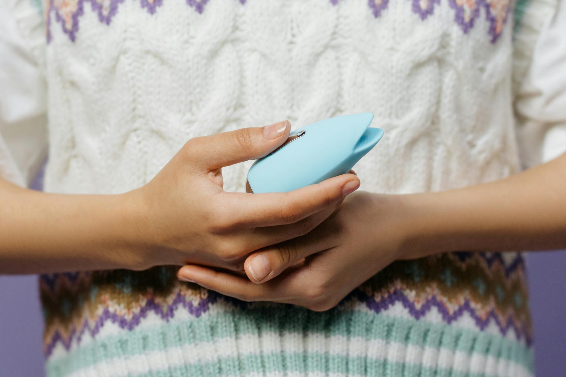 Hands holding a lemon clitoral vibrator against a cozy knitted sweater