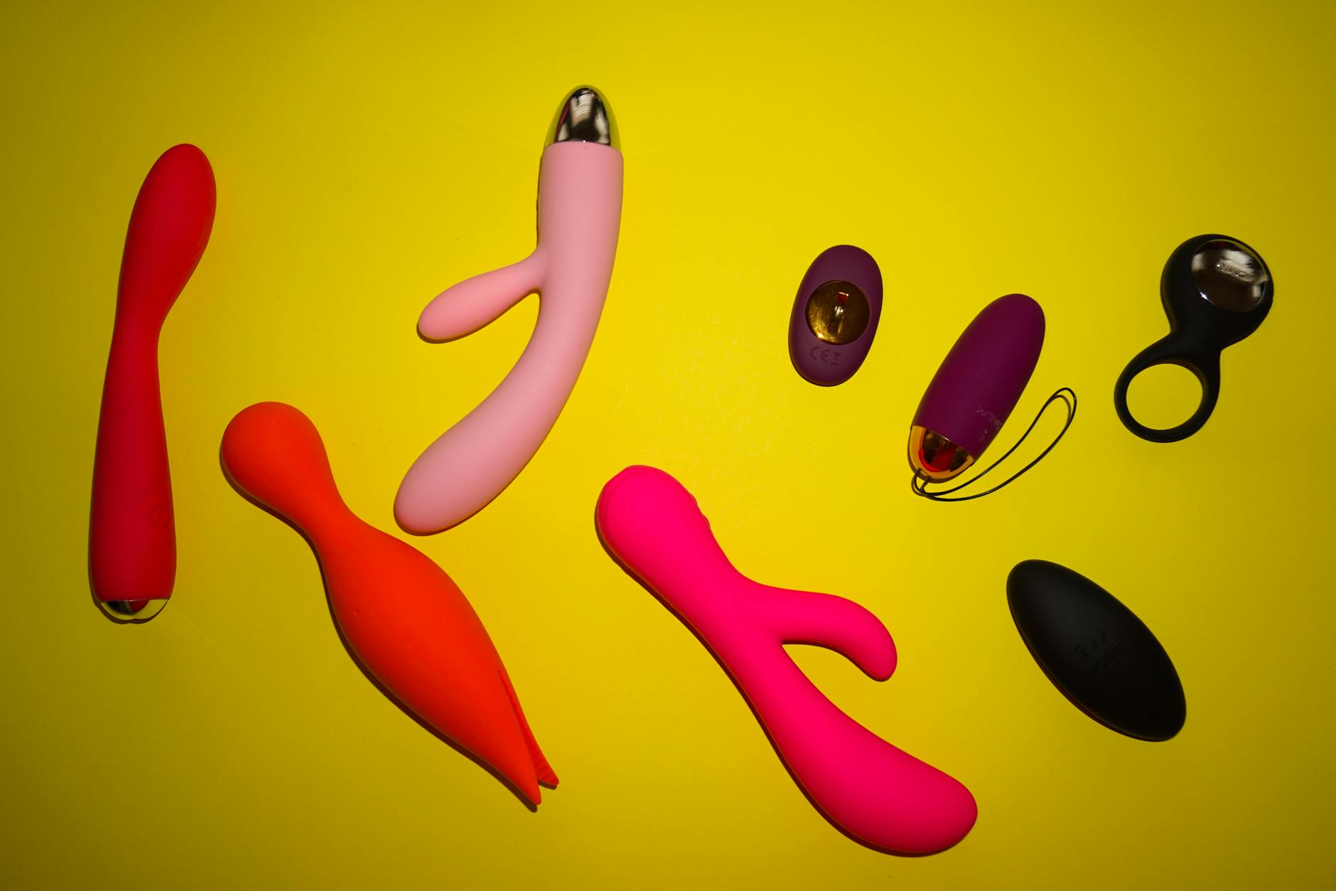 Array of colorful clitoral vibrators and suction toys displayed on a bright yellow surface