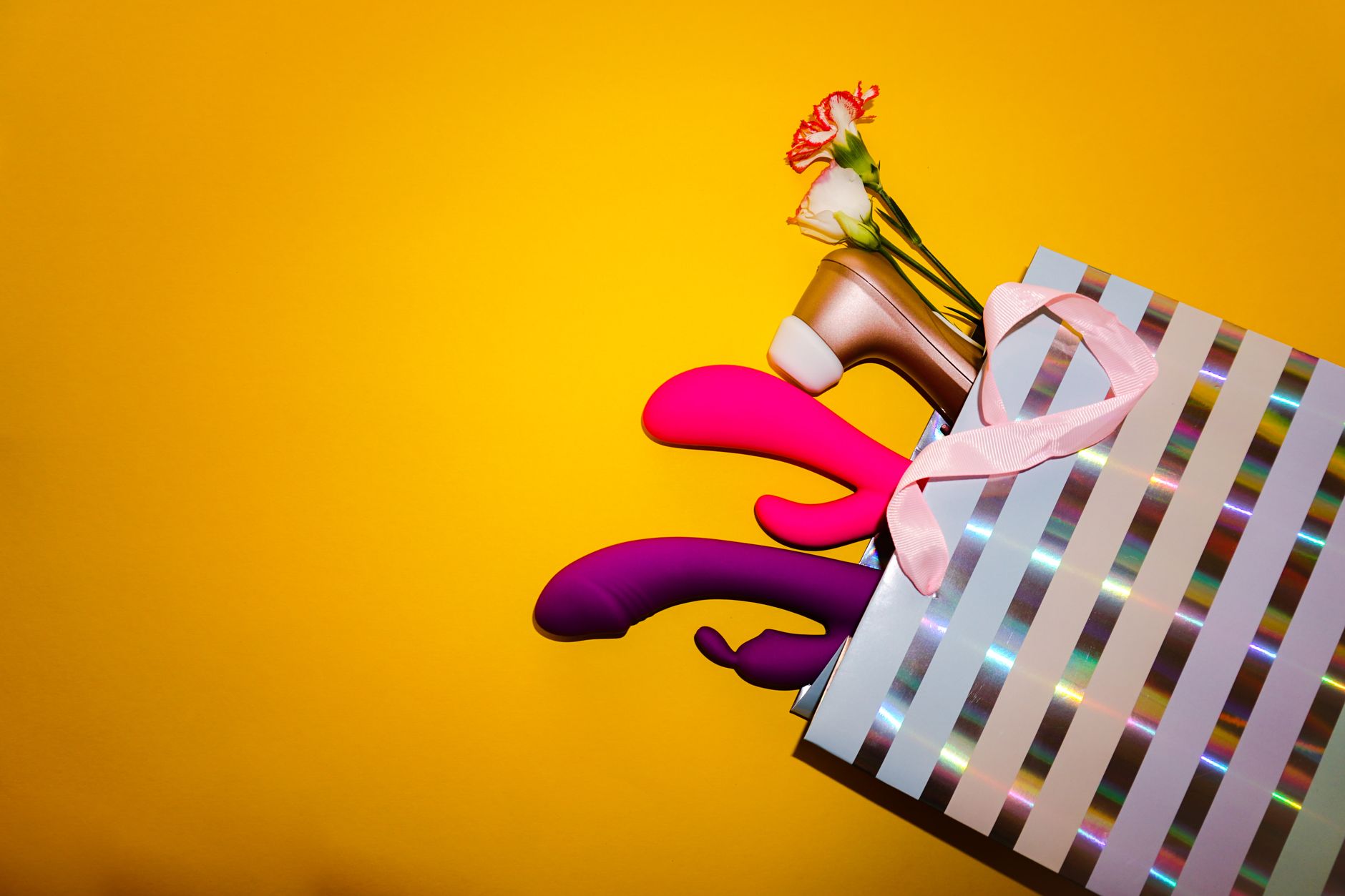 Colorful lemon vibrators and clitoral suction toys displayed with flowers in a holographic bag against a bold yellow background.
