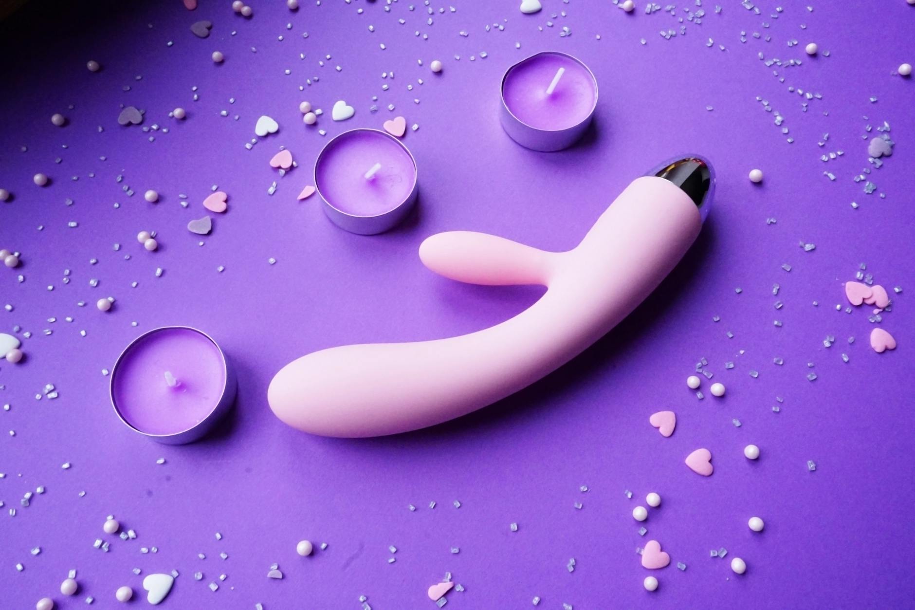 Pink vibrator on a purple background with heart confetti and candles for a romantic seasonal setting
